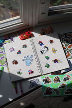 Load image into Gallery viewer, Inside pages of the JobJob Reusable Sticker BookBook filled with colorful fan art stickers — reusable waxy pages by JobJobLLC
